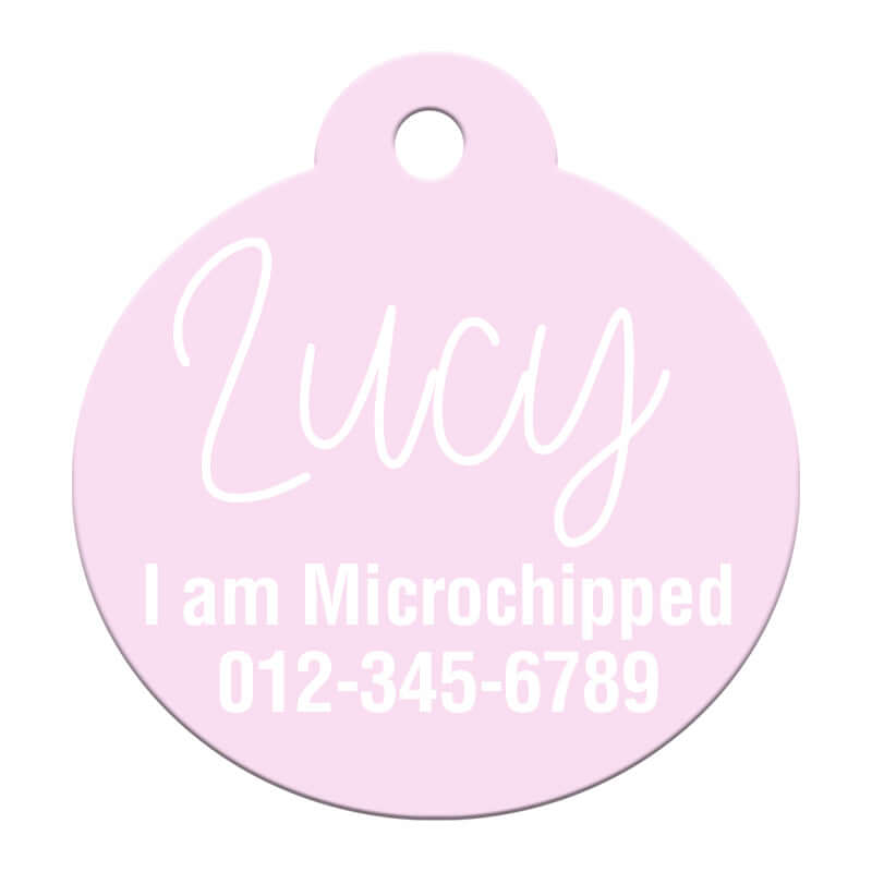 Soft pink round pet ID tag with 'Lucy' and 'I am Microchipped' message along with a contact number, designed for safety and visibility.